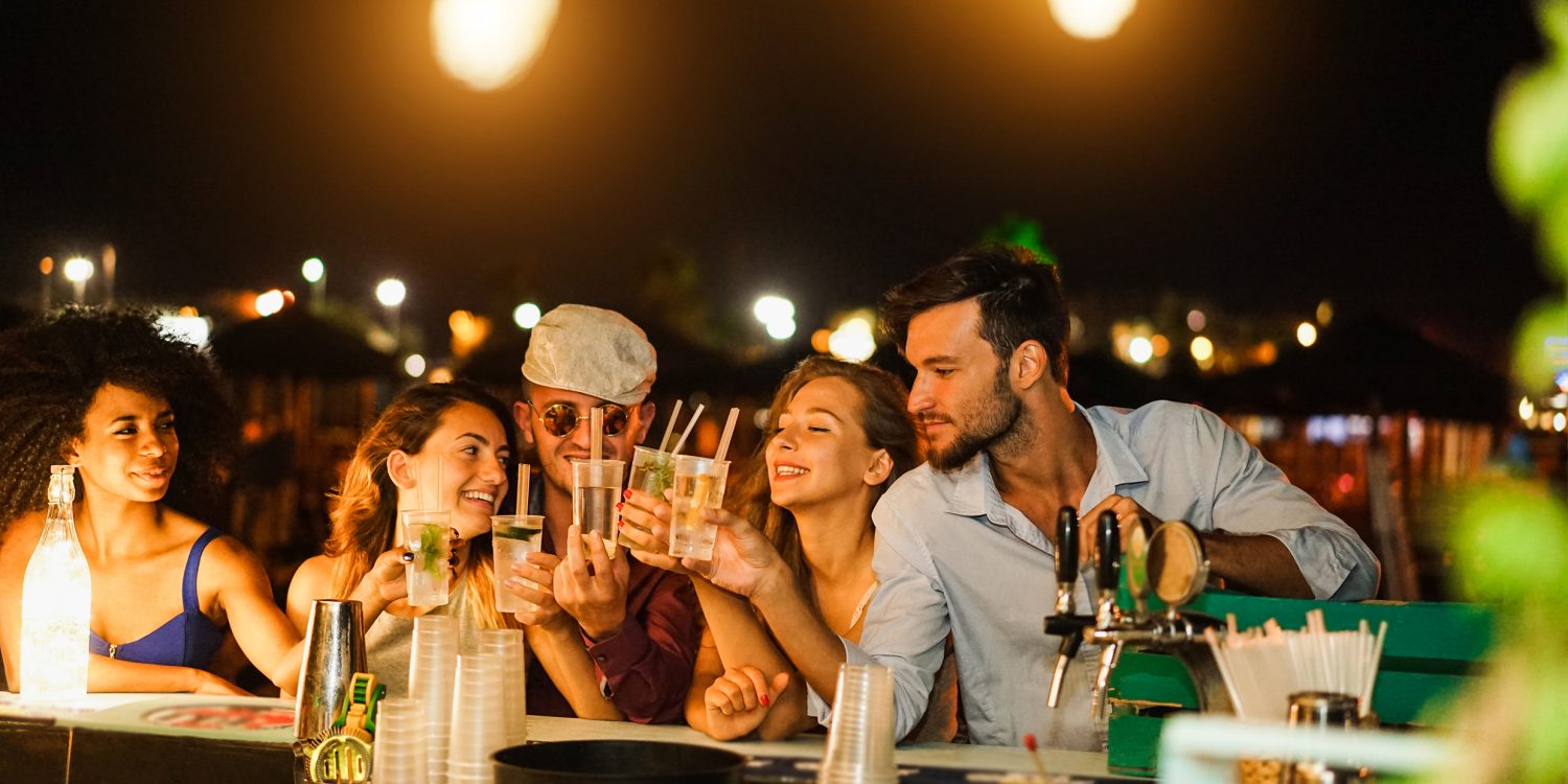 Happy friends cheering and drinking cocktails at beach party outdoor - Soft focus on right man face